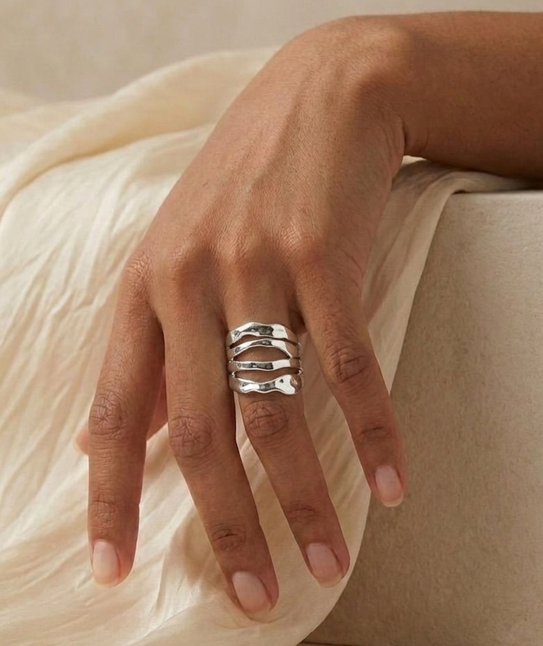 silver hammered sculptural ring on model's hand with beige fabric and stone background
