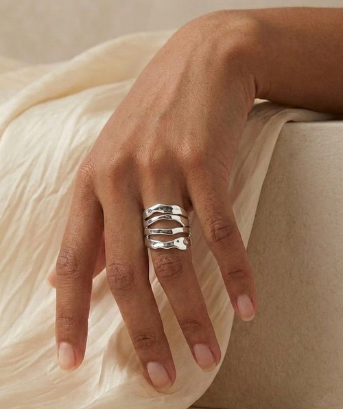 silver hammered sculptural ring on model's hand with beige fabric and stone background
