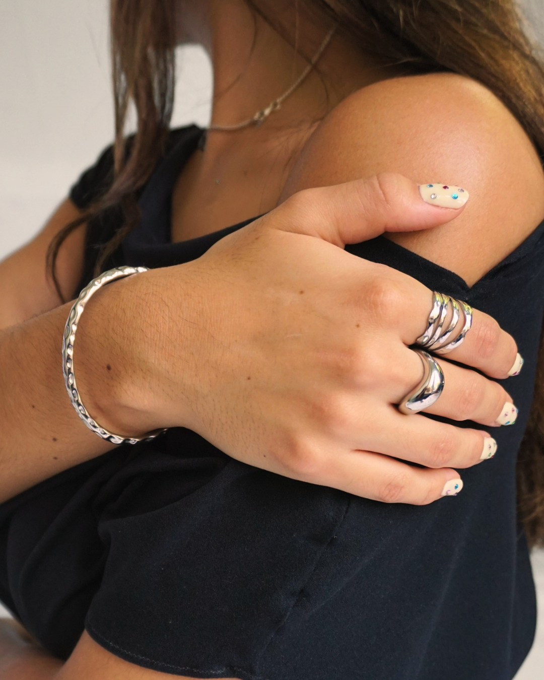 A close-up lifestyle shot of a person wearing a polished silver bangle bracelet on one wrist and multiple silver rings on one finger, paired with a black top.