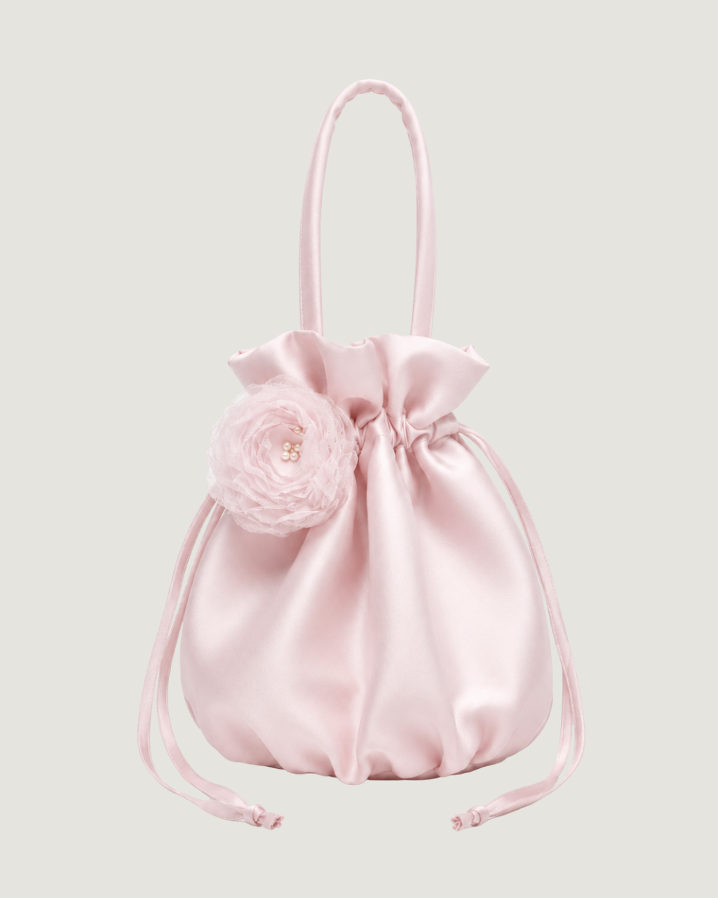 A light pink satin drawstring pouch bag with a matching top handle, featuring a decorative pink fabric flower embellishment on the front.