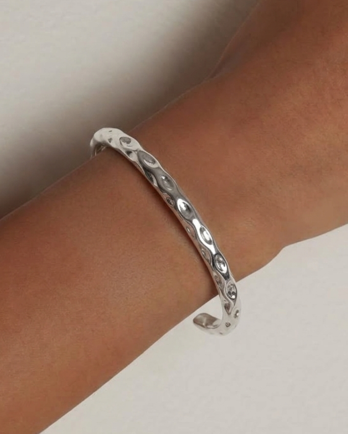 Silver bracelet on a wrist against a neutral background