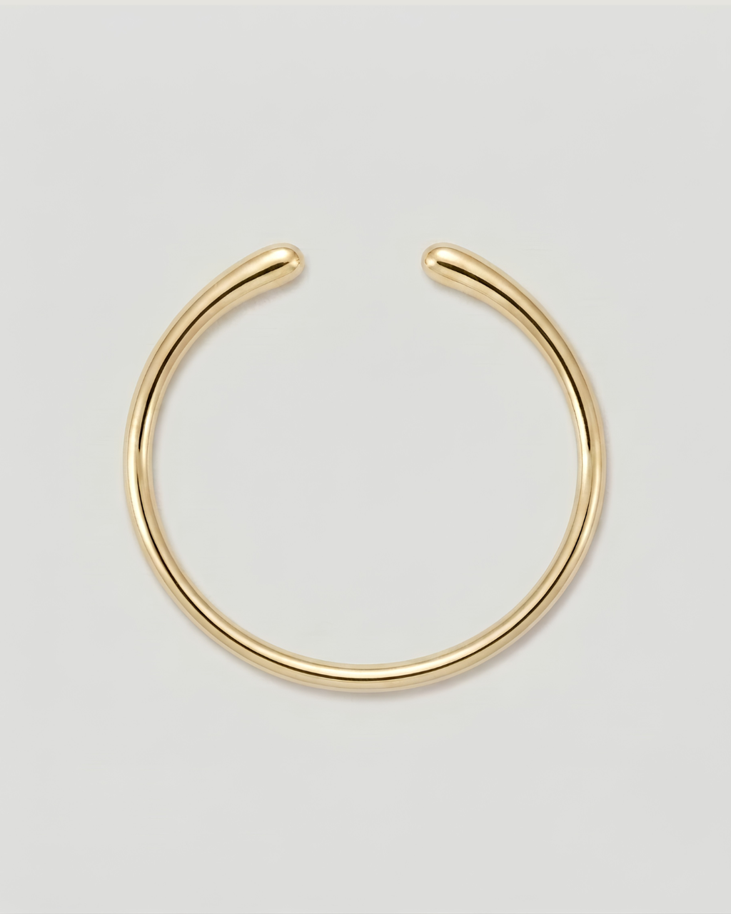 A polished gold-toned metal cuff bracelet, shown against a neutral light gray background.