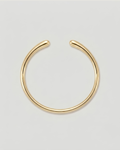 A polished gold-toned metal cuff bracelet, shown against a neutral light gray background.