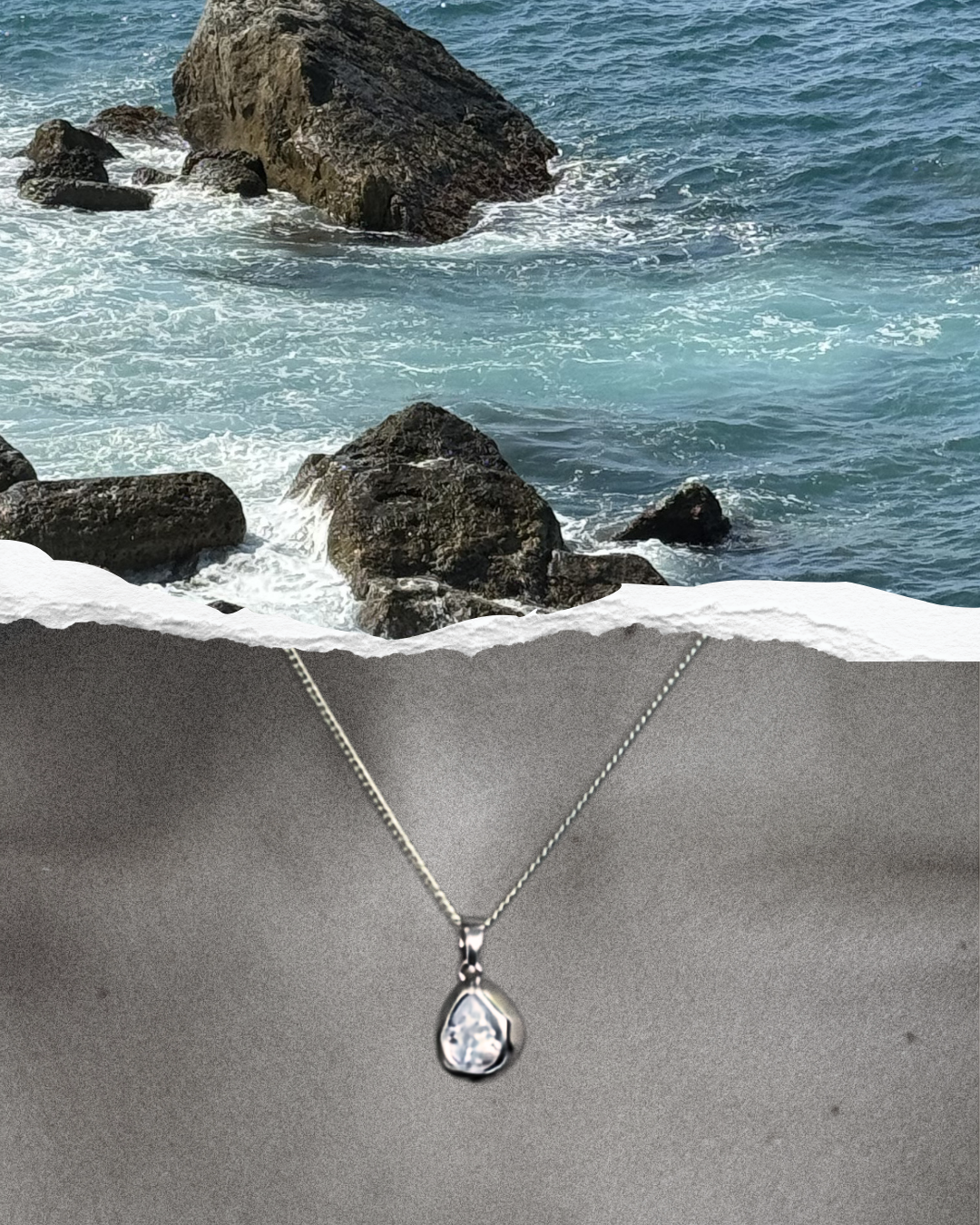 A silver chain necklace with a teardrop-shaped clear gemstone pendant, displayed against a textured gray background with a torn-paper effect revealing a rocky ocean scene above.