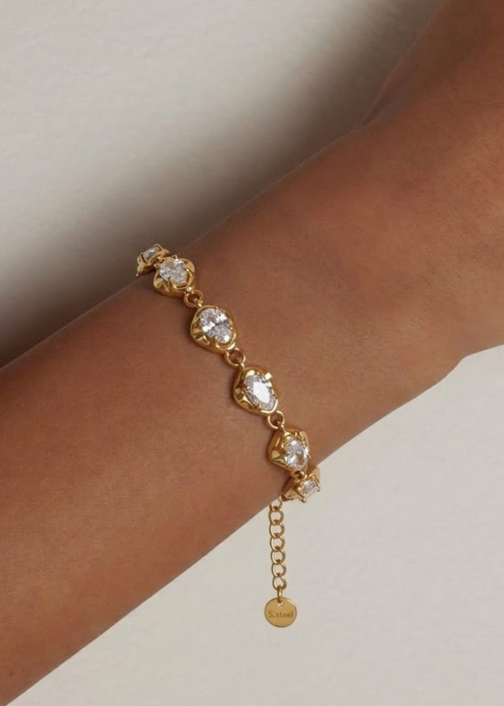 Gold bracelet with clear stones on a wrist against a neutral background