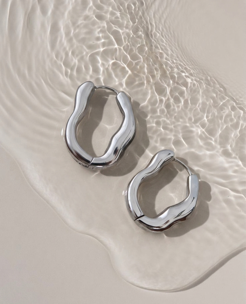 Silver hoop earrings on a sandy surface with water
