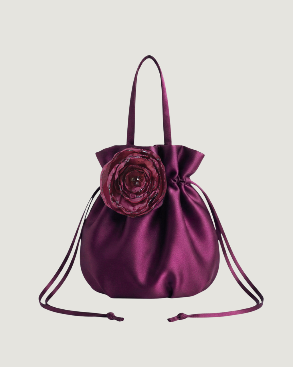 a plum satin finish drawstring bag with a handmade floral decal on the front against a beige background
