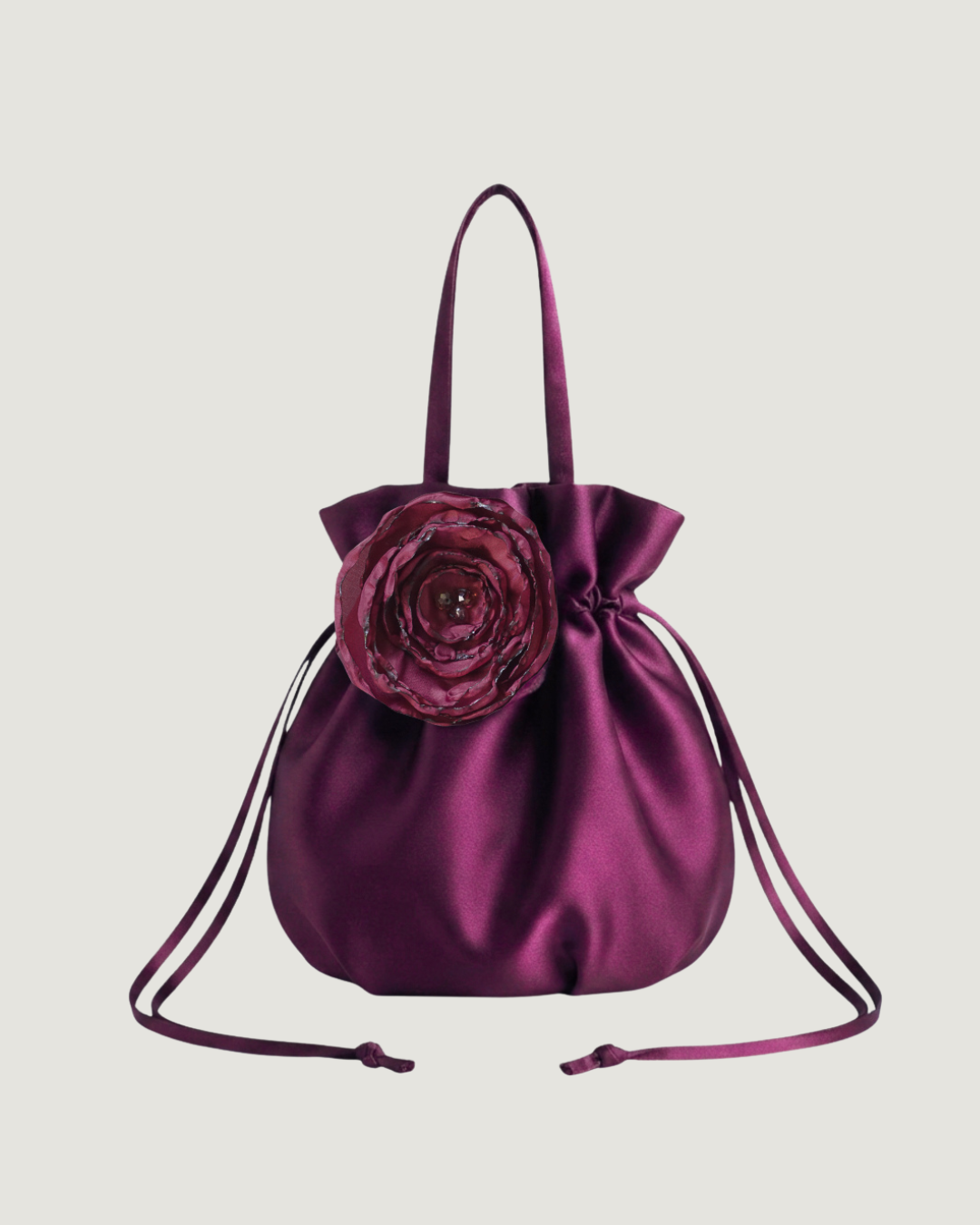 a plum satin finish drawstring bag with a handmade floral decal on the front against a beige background