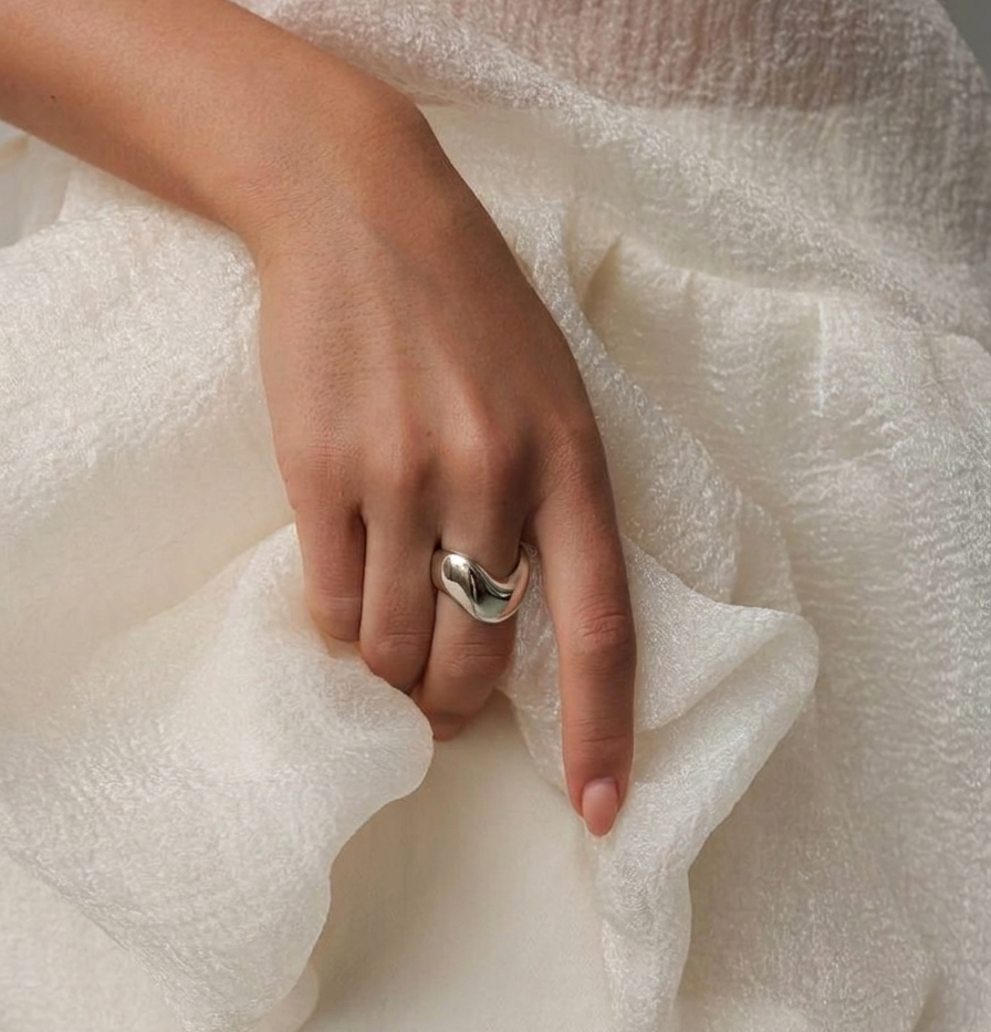 Silver ring with a modern design on a model's hand with white dress