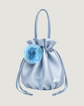 A light blue satin drawstring bag with a large light blue fabric flower accent on the front, set against a solid light beige background.