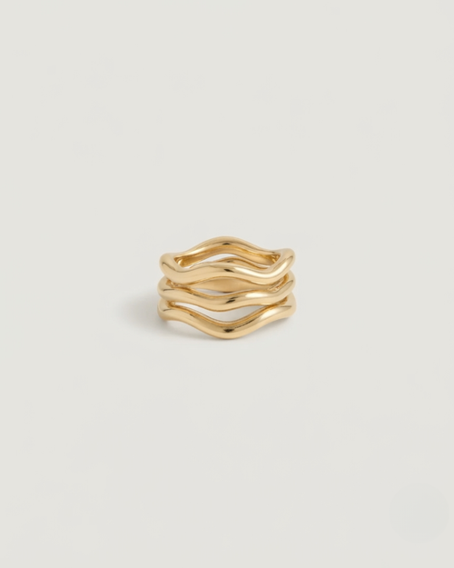 A gold wavy multi-band ring with three parallel, fluidly undulating bands, photographed on a clean, light gray background.