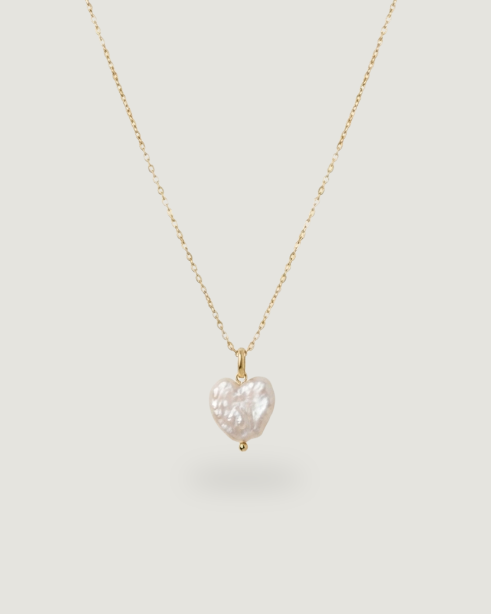 A delicate gold chain necklace featuring a small, irregularly shaped white baroque pearl pendant, displayed against a solid light gray background.