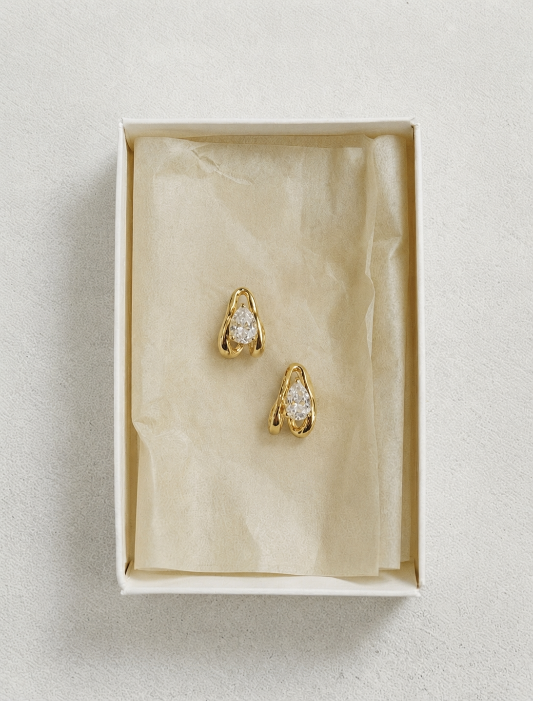Gold and diamond earrings inside tissue paper, lined gift box on a white background