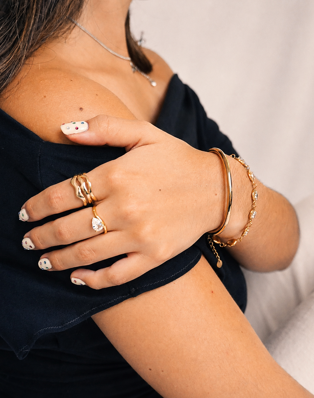gold jewelry, rings, bangles on model wearing black off the shoulder top with white background