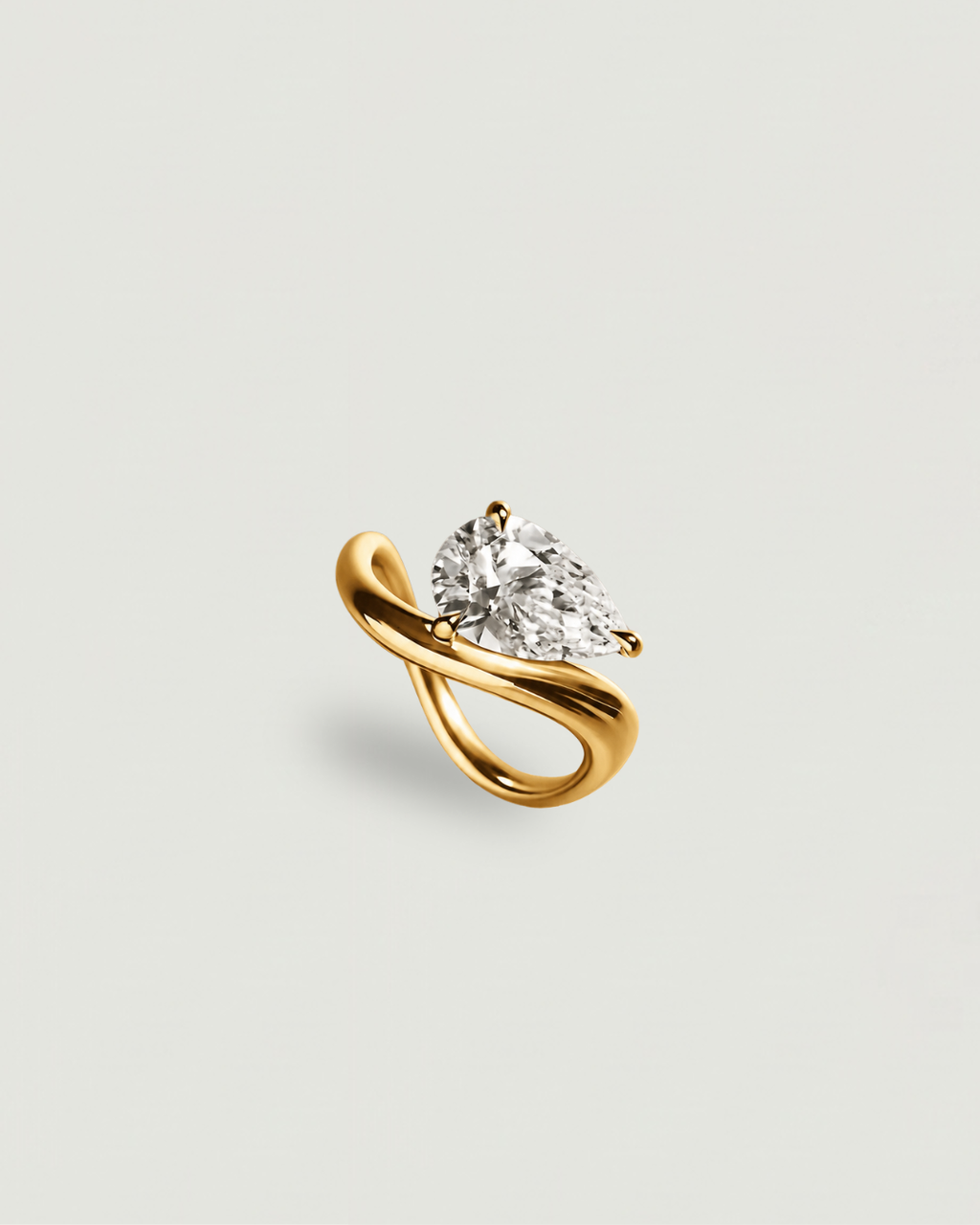 A yellow gold ring featuring a pear-cut clear gemstone in a curved, intertwined band setting, presented on a light gray background.