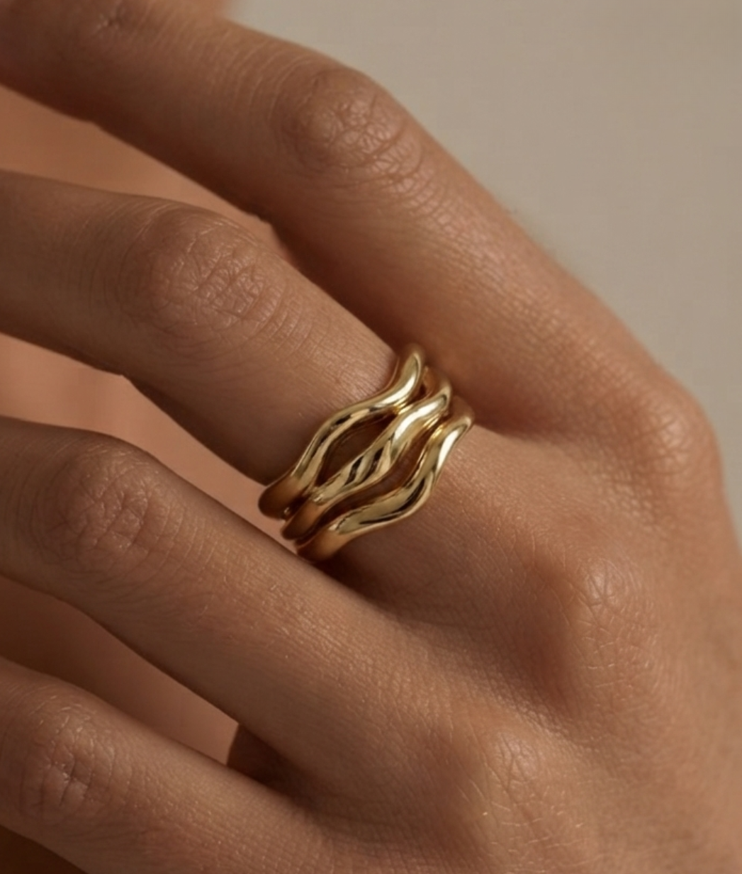 A close-up of a hand wearing a gold ring with three wavy, intertwined bands.