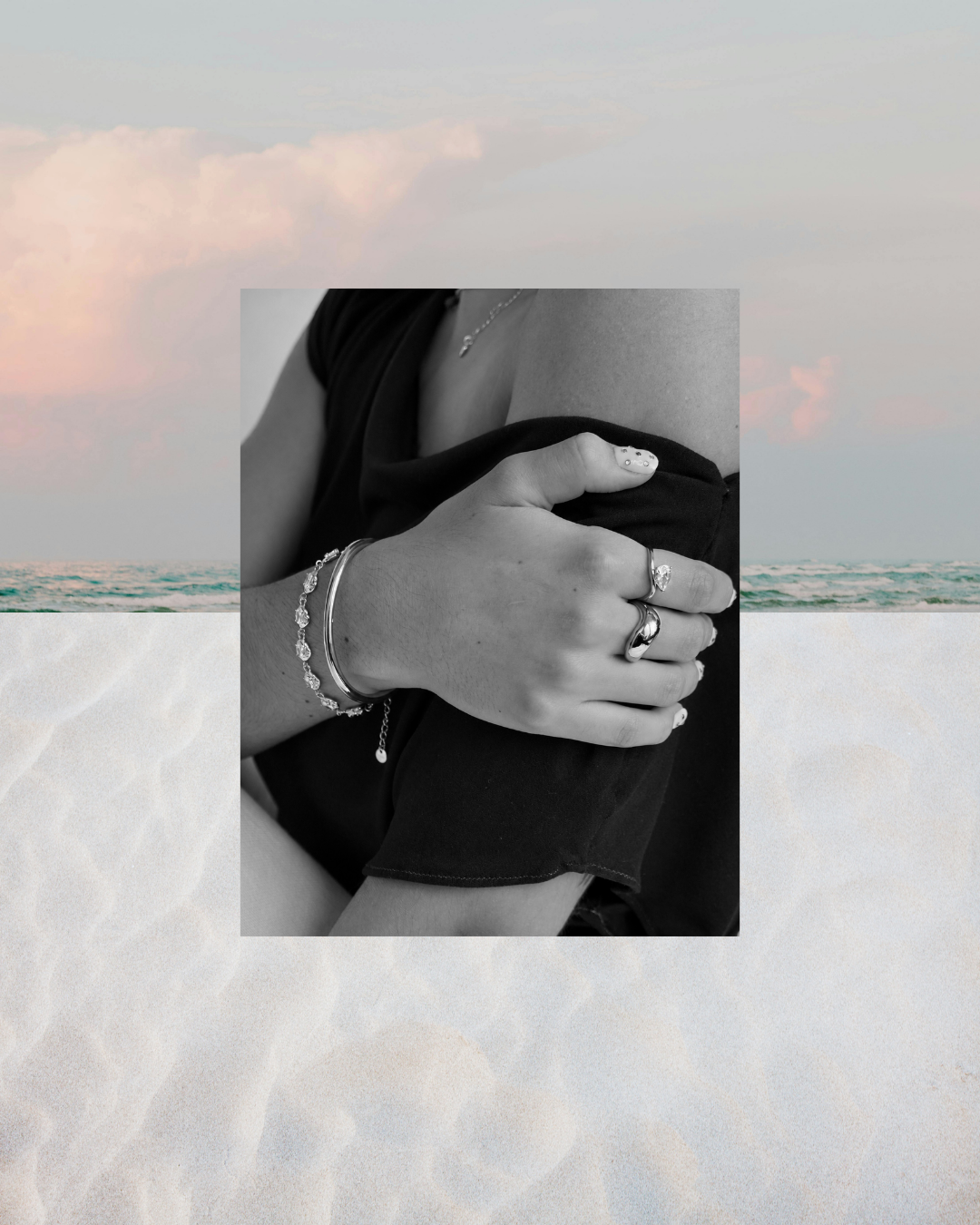 A black and white close-up of a person's hand wearing silver bracelets and rings, overlaid on a beach background with sand and ocean.