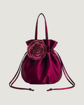 A deep magenta satin drawstring bucket bag with a large matching fabric flower accent on the front, set against a plain light gray background.