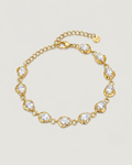 A gold chain bracelet with nine heart-shaped bezel settings containing clear round-cut stones, displayed on a light beige background.