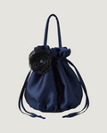 A navy blue satin drawstring pouch bag featuring a large black fabric flower accent on the front and dual top handles, set against a solid light gray background.