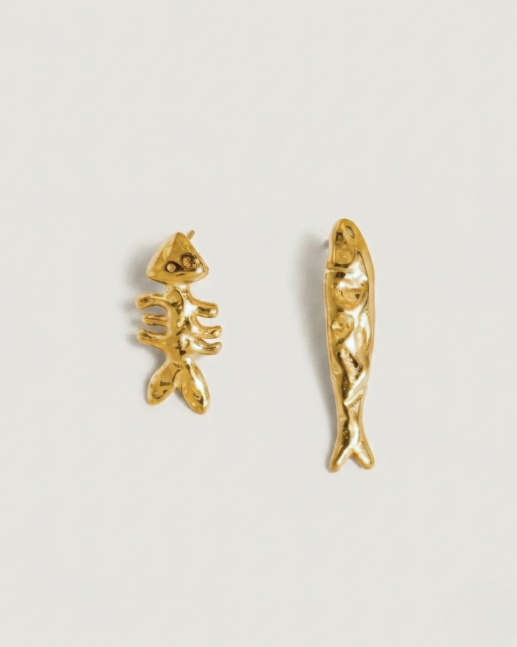A pair of gold fish-shaped stud earrings on a light gray background.