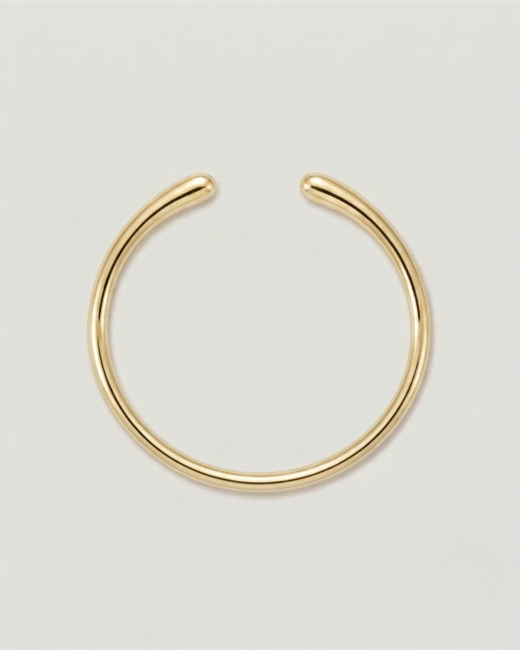 A minimalist gold-toned metal hoop earring with an open, curved design, displayed on a clean light gray background.