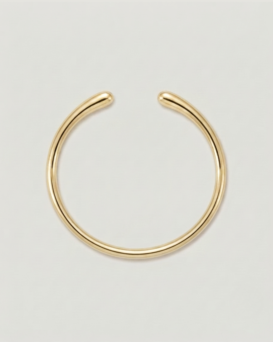 A minimalist gold-toned metal hoop earring with an open, curved design, displayed on a clean light gray background.