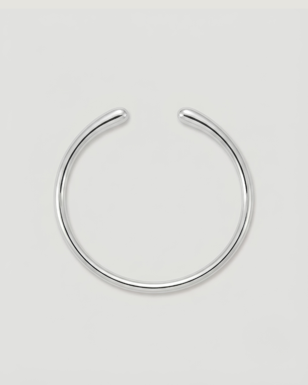 A minimalist silver-toned metal cuff bracelet, shown on a neutral light gray background.