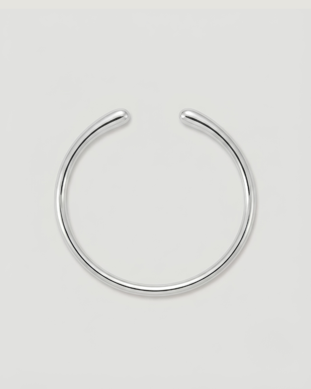 A minimalist silver-toned metal cuff bracelet, shown on a neutral light gray background.