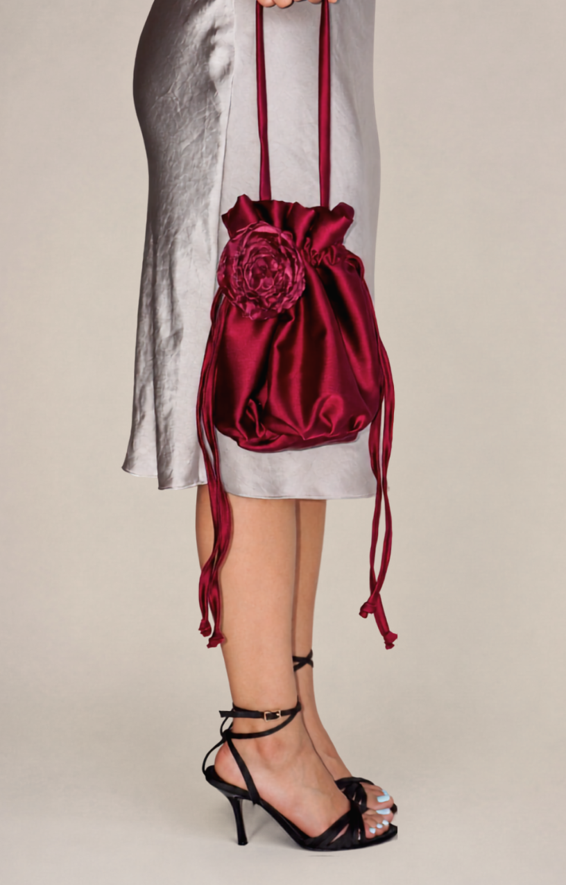 raspberry red satin bridal bag with handmade magenta silk organza flower attached, being held by model wearing a long taupe satin dress wearing black strappy heels on a beige background